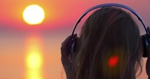 Girl listening to music and looking at sunset scene