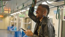 Young man holds smartphone and smiling while traveling by subway. Black man in headphones with phone.
