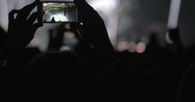 Hands in the crowd holding smart phone and shooting musical performance. Bright illumination on the stage