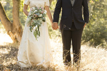 torsos of a bride and groom holding hands outdoors 