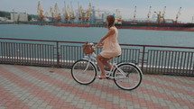 Blonde lady with hipster retro bike in stylish dress. Woman enjoying summer day. Riding bicycle in sea port