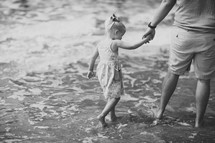father and daughter walking holding hands on a beach 
