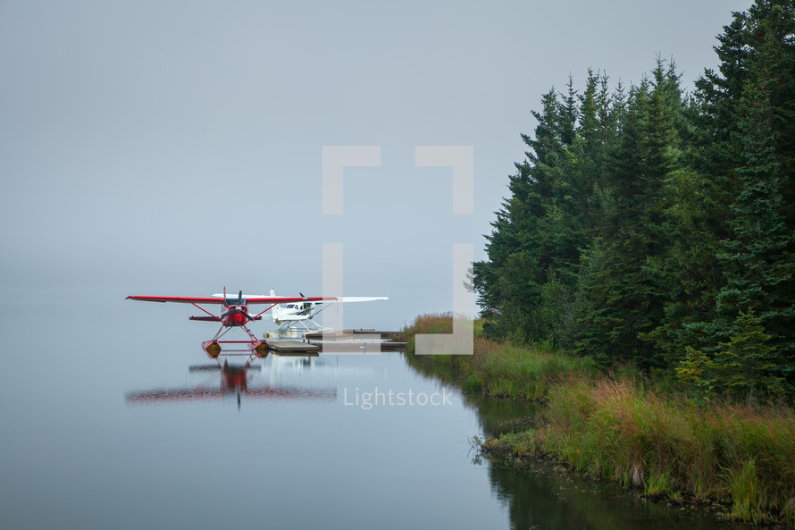 Two Alaskan red and white float airplanes on edge of river 