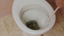 Man's hand with brush cleaning a dirty toilet