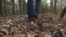 man walking through fall leaves in a forest 