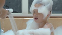 Mother washing foam from child in the bath