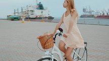 Blonde lady with hipster retro bike in stylish dress. Woman enjoying summer day. Riding bicycle in sea port