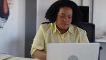 Focused businesswoman typing at modern laptop and talking on the phone in office interior close up. 
