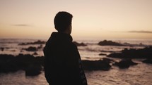 young man standing near the ocean deep in thought 