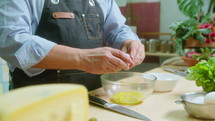 Senior male chef in apron whisking eggs in glass bowl and talking, filming video recipe or cooking vlog in the kitchen
