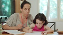 Mother helping her little daughter to prepare homework at home