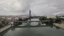 Drone pullback over Guadalquivir river, past colorful and quaint Triana, Seville