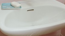 A man's hand cleaning a bathroom sink with brush