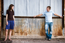 man and woman leaning against a ware house wall talking