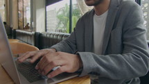 Midsection cropped shot of businessman typing on laptop at cafe table while doing remote job
