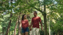 Young positive latin couple walking holding hands date in summer city park. Man and woman enjoying spend time together