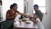 Family making breakfast while husband and little son eating and drinking juice at kitchen table