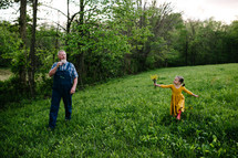 grandfather and granddaughter walking through a field of green grass