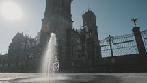 Fountain spouting from the ground with in the background a beautiful entrance gate of the great cathedral Bascilica de Puebla in Mexico. Slow motion panning shot