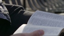 man reading a Bible on a bench 