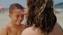 mother applying sunblock lotion on sons skin for sun protection little boy getting ready to swim on the beach with mom using sunscreen caring for childs health on sunny day 