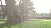 a man reading a Bible standing under a tree in a park 