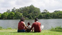 back view of Little boy sitting with father and mother over the lake at city park. Family outdoors, happy parenting and childhood, kids and parents relaxing outside
