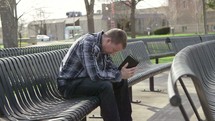a man sitting on a bench praying holding a Bible 