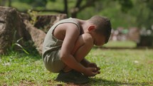 The child is depressed. Childhood loneliness. A depressed boy sits on the grass at the park
