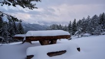 A snowy wooden tourist bench, a lot of snow in the forest, cloudy winter weather