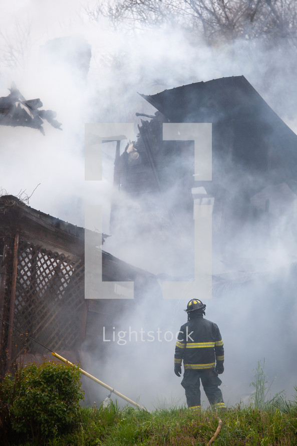 Fire fighter standing in front of burning smokey building on fire 