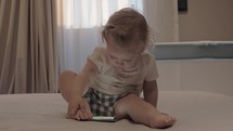 A baby girl sitting on a bed with a tablet in front of her