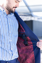 A man opening his jacket to reveal sunglasses and red paisley lining.