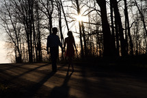 couple walking holding hands down a dirt road at sunset 