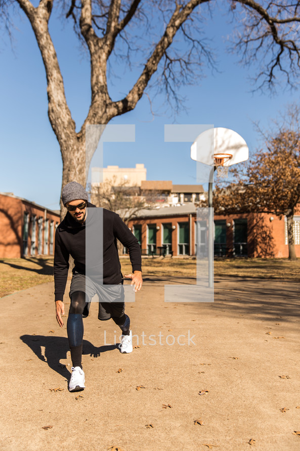 A man exercising outdoors near a basketball goal.