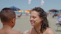 son helping mother to apply sunblock lotion on a playful way. Summer time family enjoying beach day