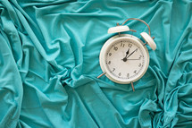 White alarm clock on a teal fabric background 