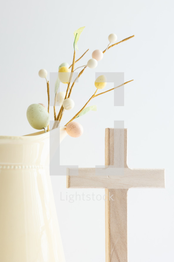 Decoration sprig with easter eggs and cross in a yellow pitcher with copy space