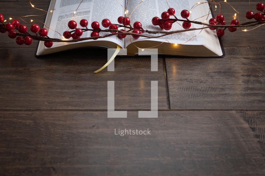 open BIble, red berries and fairy lights on a wood background 