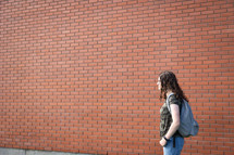 a teen girl with a bookbag standing in front of a brick wall 