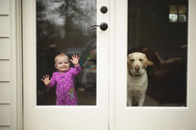 a dog and toddler standing at a back door window 
