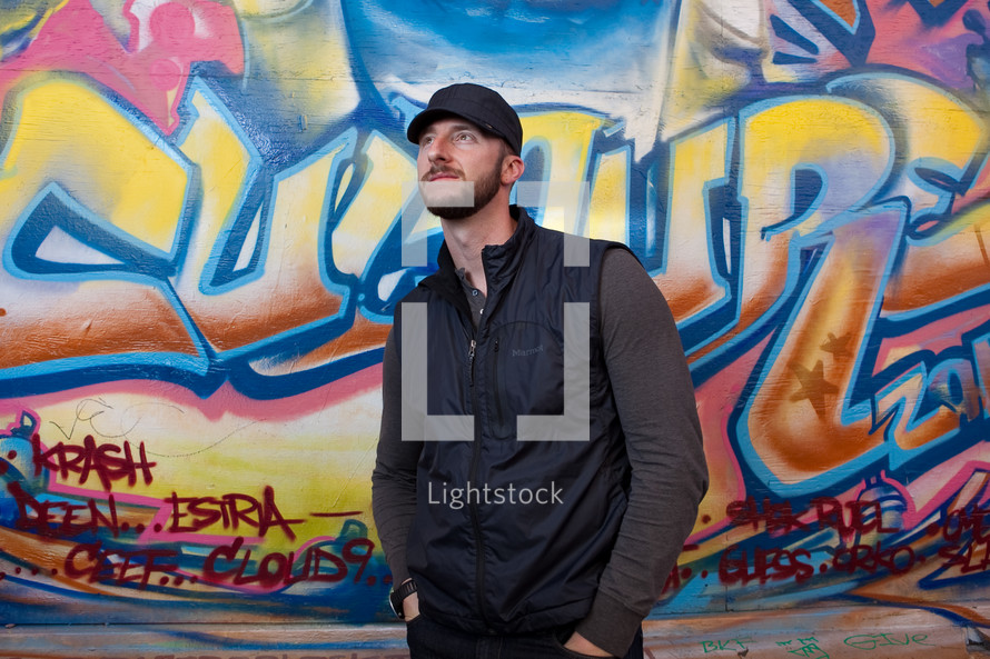 man standing in front of a wall covered in graffiti 