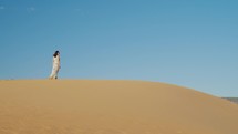 Traveler woman leaving footprints on sand dune at golden sunset. 