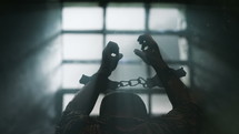 Prisoner with chained hands pray to the Lord. View trough prison window. 