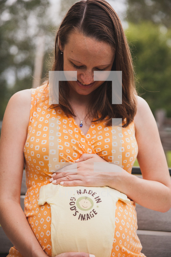 pregnant woman with a made in God's image onesie over her belly