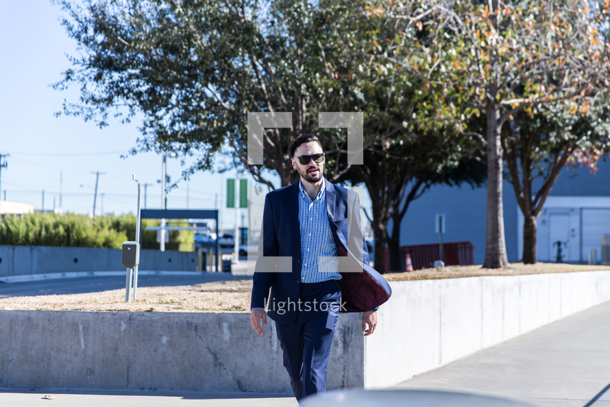 man in a sports coat and sunglasses walking in a city 