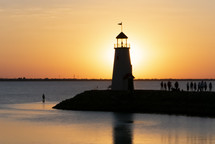 silhouettes of lighthouse and people gathered nearby at sunset with beautiful orange and yellow sky