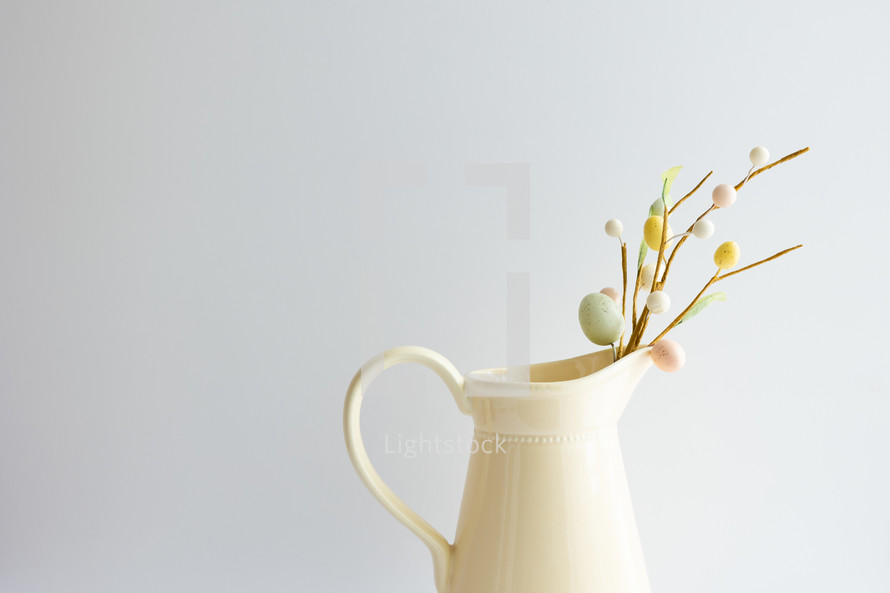 Decoration sprig with easter eggs in a yellow pitcher with copy space