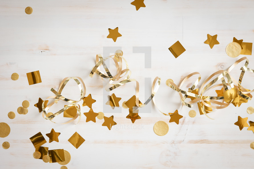 Gold confetti and streamers on a white wood background with copy space
