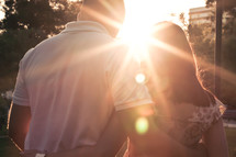 Couple with arms around each other's backs with sun beam shining between them.